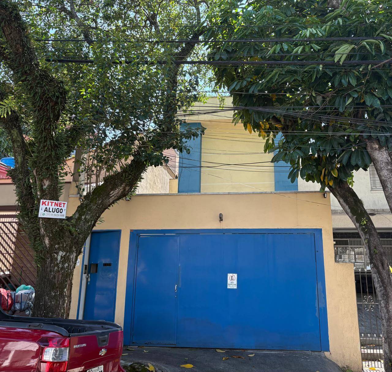 Fachada de kitnet disponível para alugar em Pinheiros, São Paulo, com portão azul e árvore na calçada